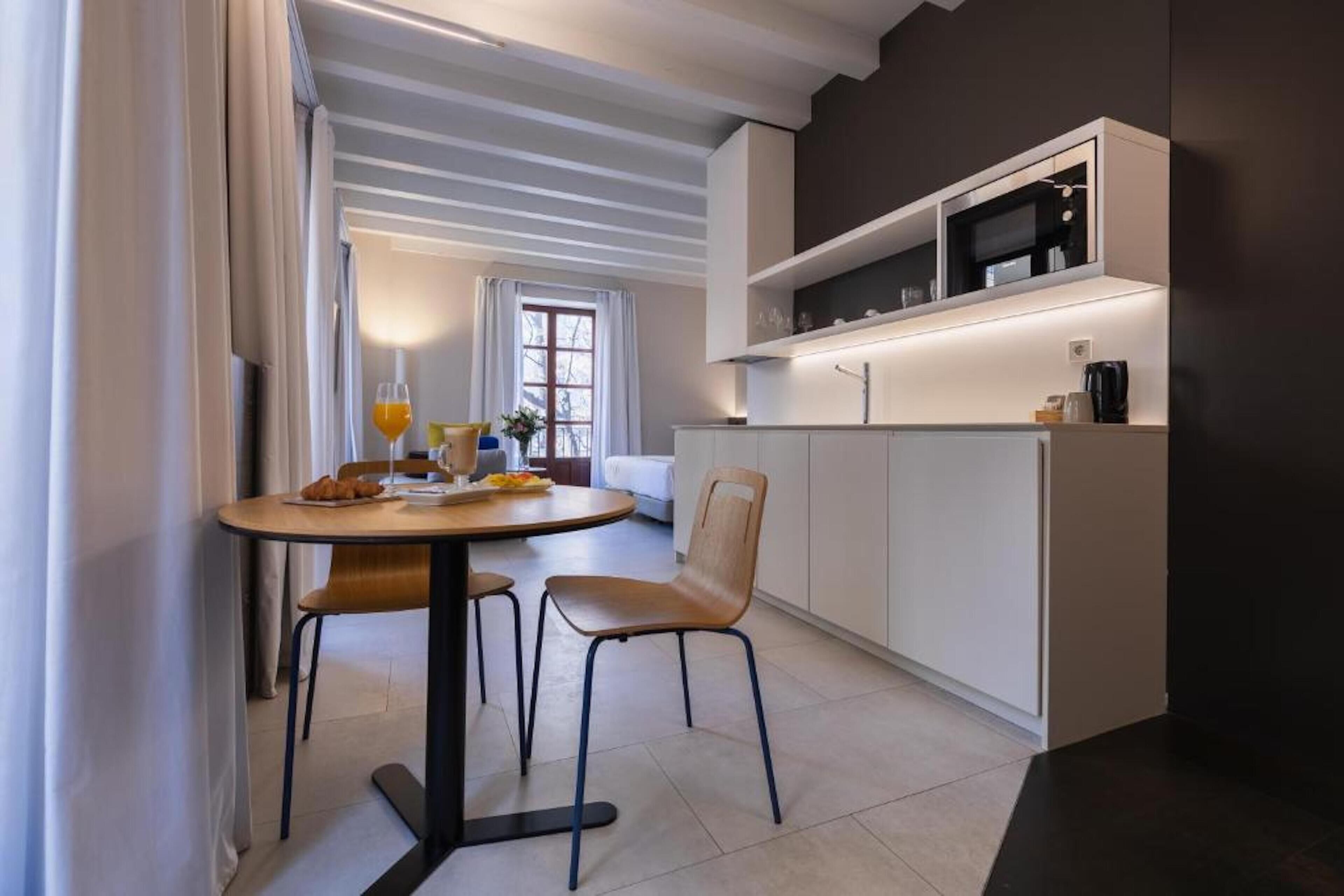 Cocina moderna con armarios blancos, microondas y cafetera. Cuenta con un comedor con una mesa redonda y dos sillas.