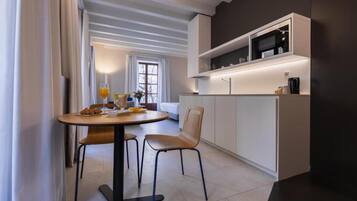 Cocina moderna con armarios blancos, microondas y cafetera. Cuenta con un comedor con una mesa redonda y dos sillas.