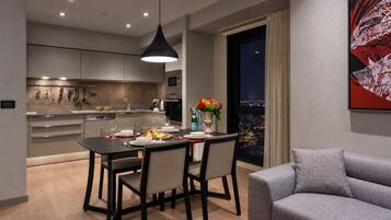 A modern dining area with a table set for two, a grey sofa, and a cityscape view through a large window.