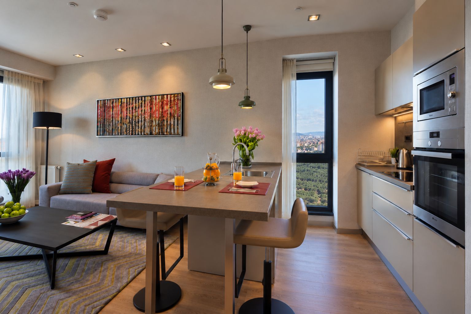 A modern kitchen with a built-in oven and microwave, a dining area with a table and chairs, and a sofa with a view of the city.