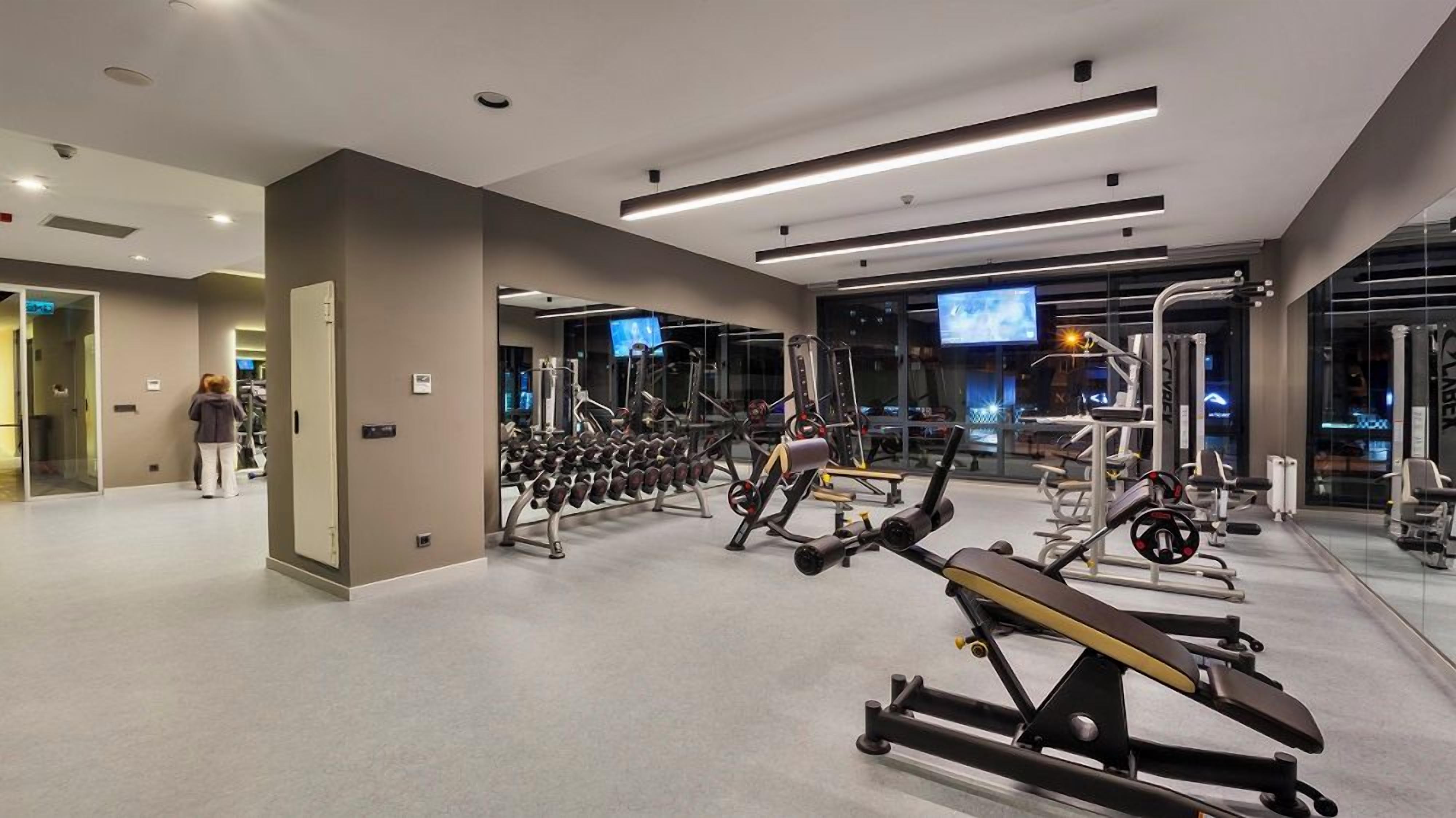 Een sportschool met diverse fitnessapparaten, een televisie en een persoon in beweging.