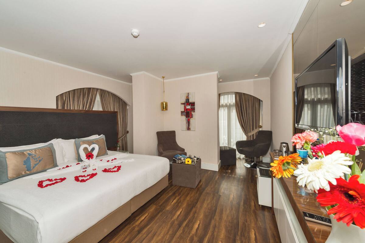 A hotel room with a bed, a desk, a chair, a TV, and a vase of flowers.