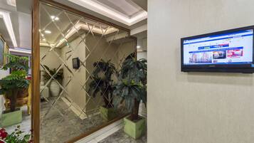 Un área de recepción con un panel espejado, un televisor montado mostrando una página web y plantas en macetas.
