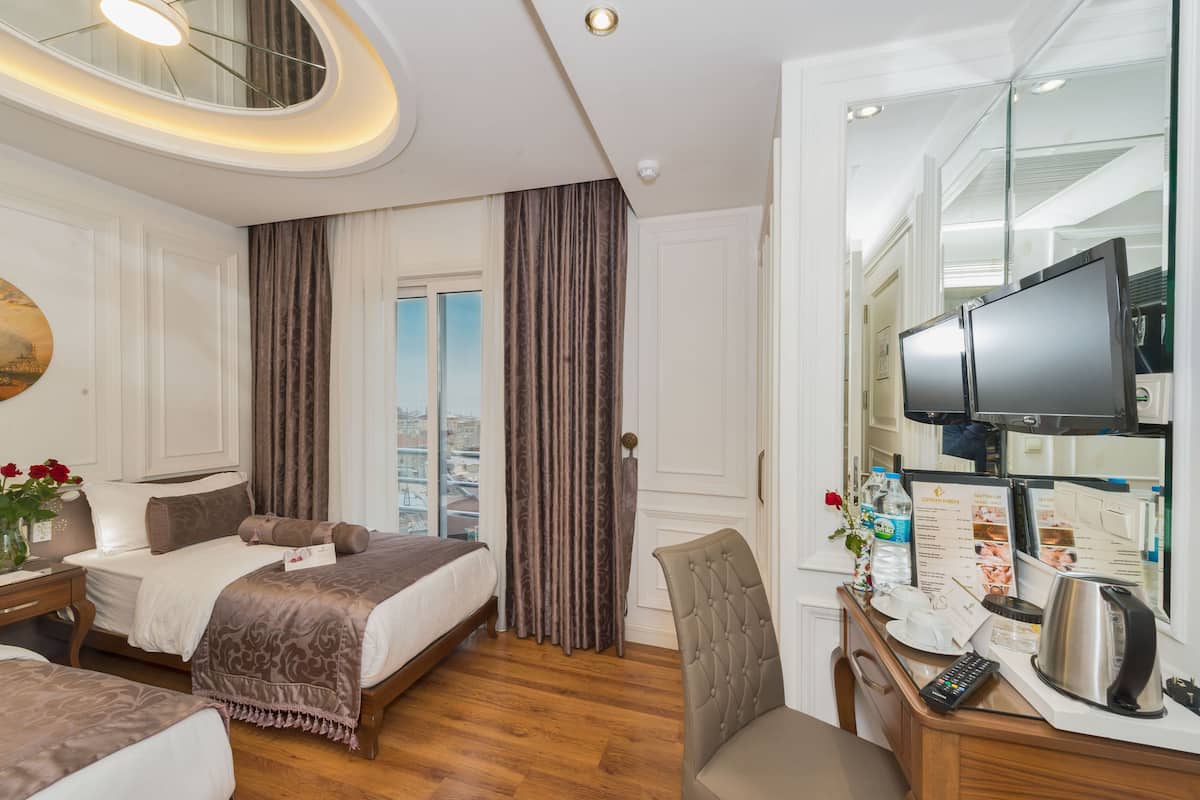 A hotel room with a bed, a desk with a television, a chair, and a city view through the window.