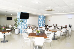 A spacious dining area with multiple tables and white chairs, featuring blue and white floral wall designs and potted plants.