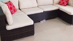 Un sofá modular con estructura de mimbre oscuro y cojines color crema, adornado con almohadones estampados en rojo.