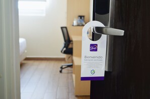 A hotel room door with a sign indicating it is a "Sleep" brand room, featuring a clean, minimalistic design with a wooden floor and a black office chair in the background.