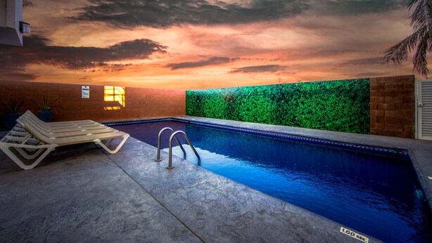 Una piscina interior con vista al atardecer, una tumbona y una pared verde.
