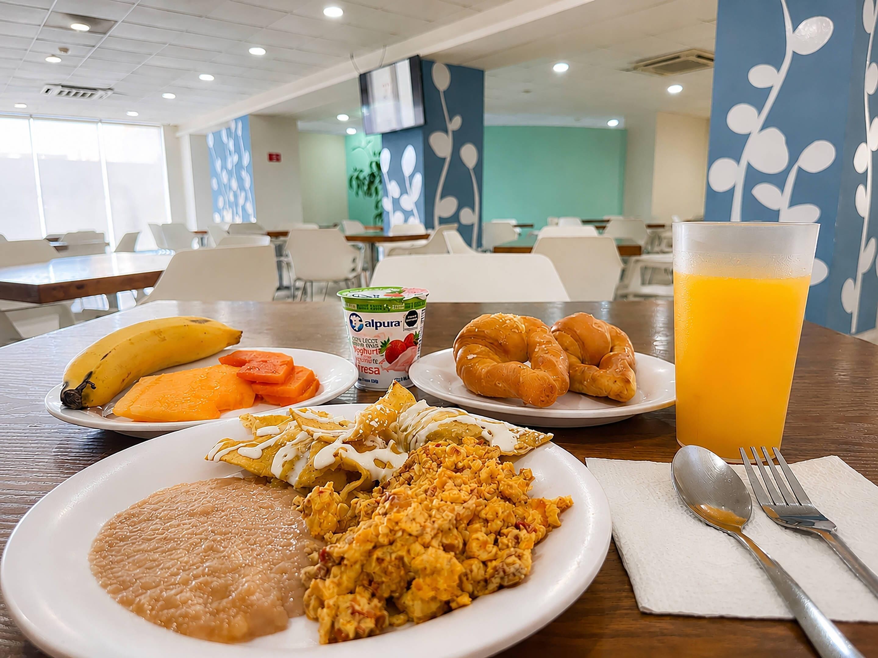 A breakfast setting with plates of food, a glass of orange juice, and a yogurt container.