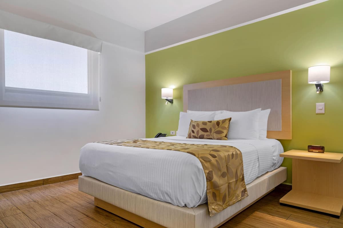 A hotel room with a bed, bedside lamps, a nightstand, and a window.