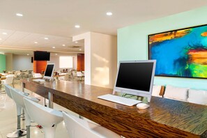 A modern hotel lobby with a long reception desk, multiple computer monitors, and a large abstract painting on the wall.