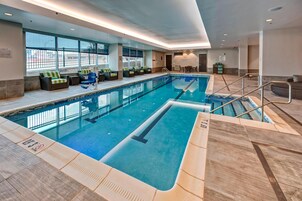 Una amplia piscina cubierta con marcas claras de carriles, una zona de estar con sillones acolchados y vistas al exterior a través de grandes ventanales.