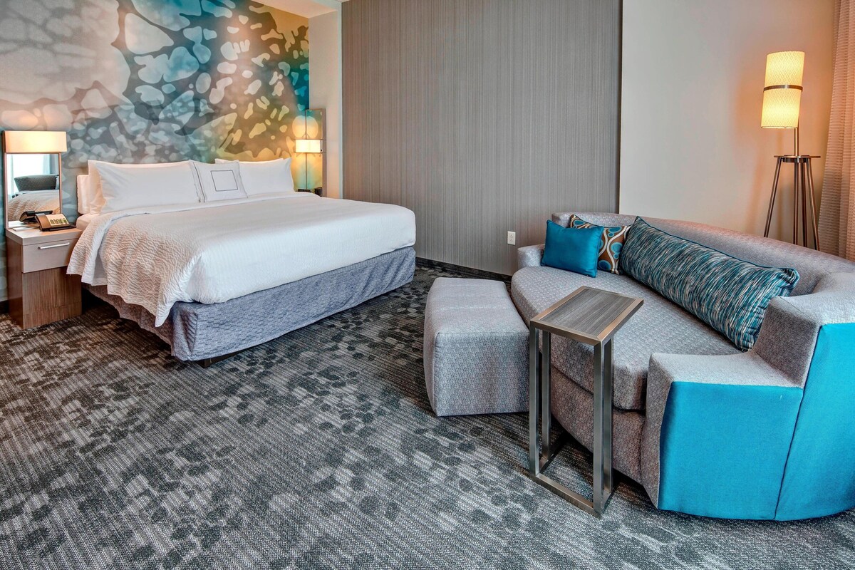 A hotel room with a large bed, a sofa, a small table, and a lamp.