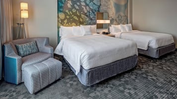 A hotel room with two beds, a sofa, a standing lamp, and a large abstract wall mural.