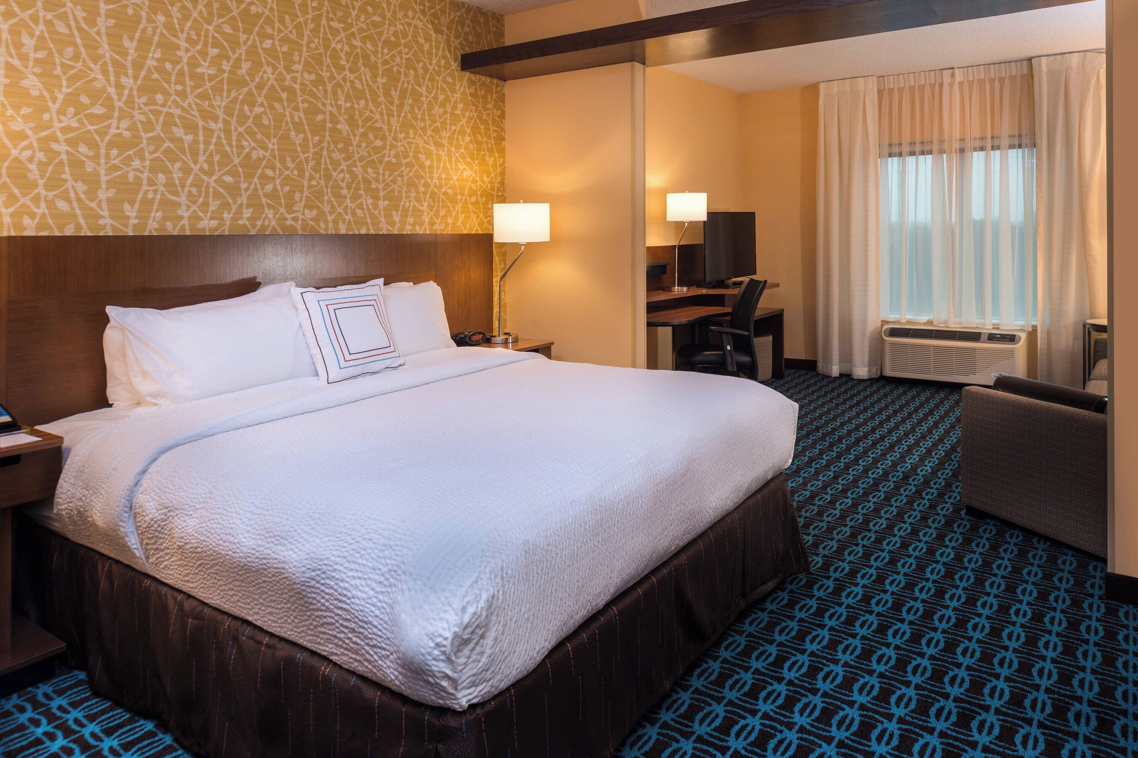A hotel room with a large bed, a desk, a chair, and a separate bathroom area.