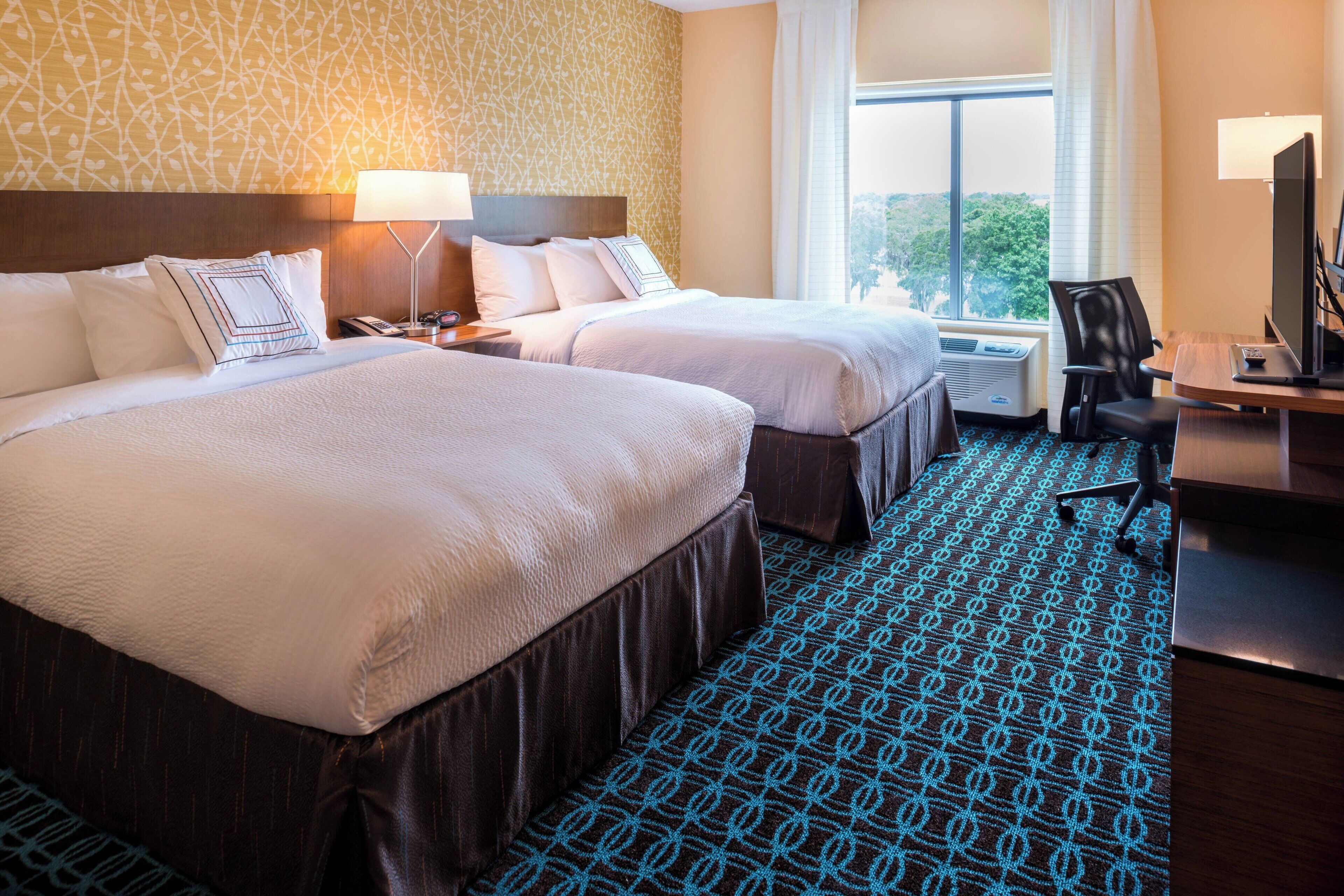 Quarto de hotel com duas camas, uma secretária com computador e janela com vista.