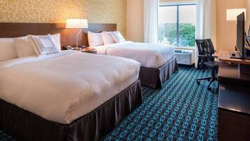 Quarto de hotel com duas camas, uma secretária com computador e janela com vista.