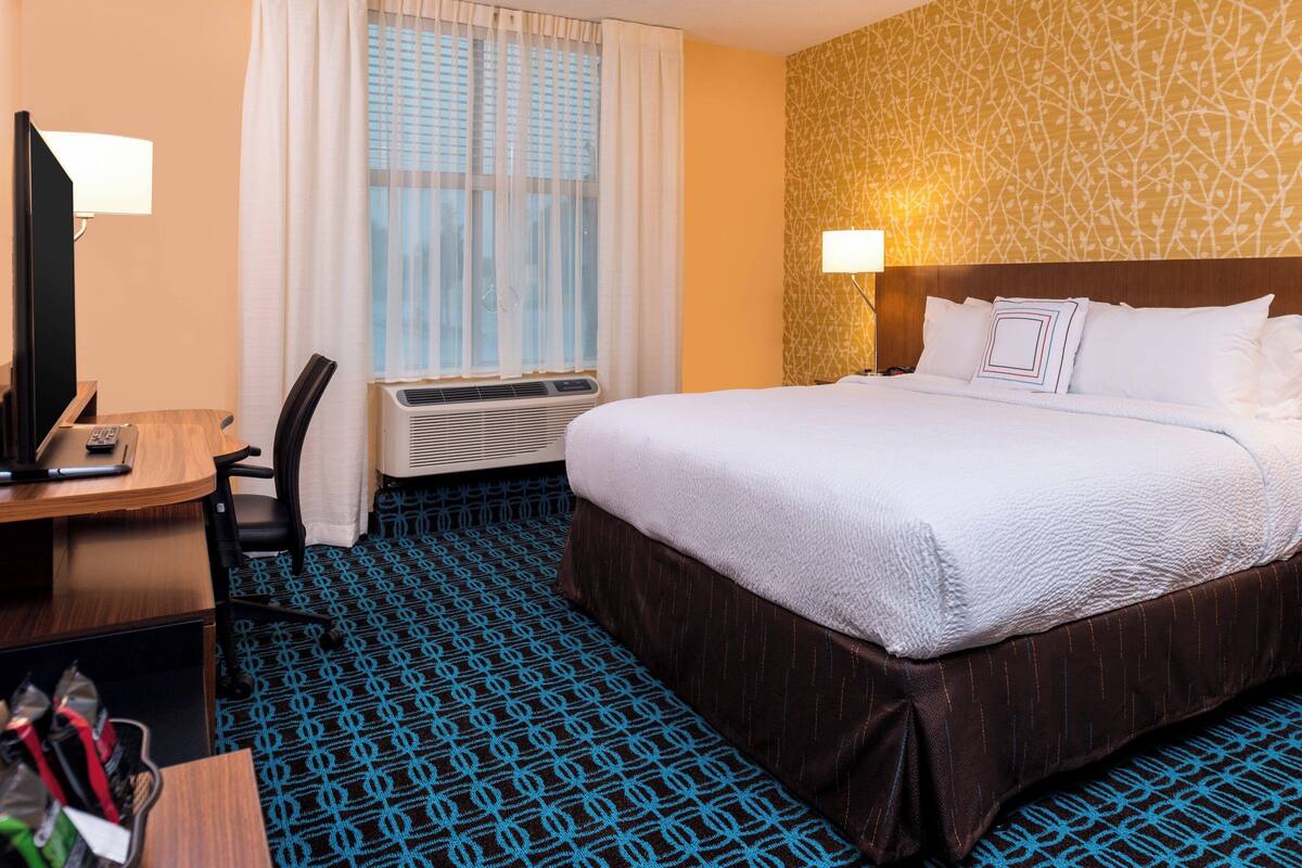 Une chambre d’hôtel avec un grand lit, un bureau avec une chaise, une télévision et un appareil de climatisation.