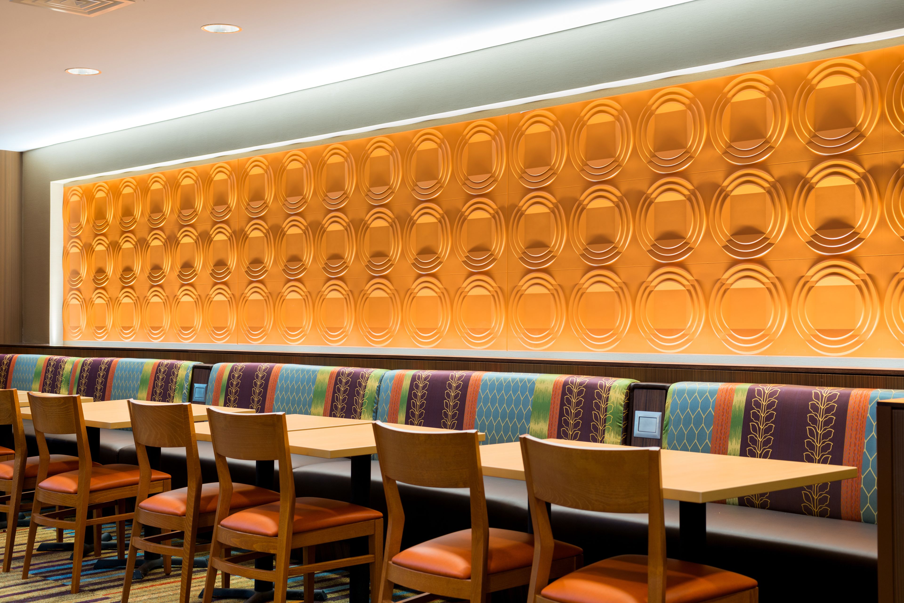 A restaurant with wooden tables and chairs, a colorful bench seating area, and a wall with a circular pattern.