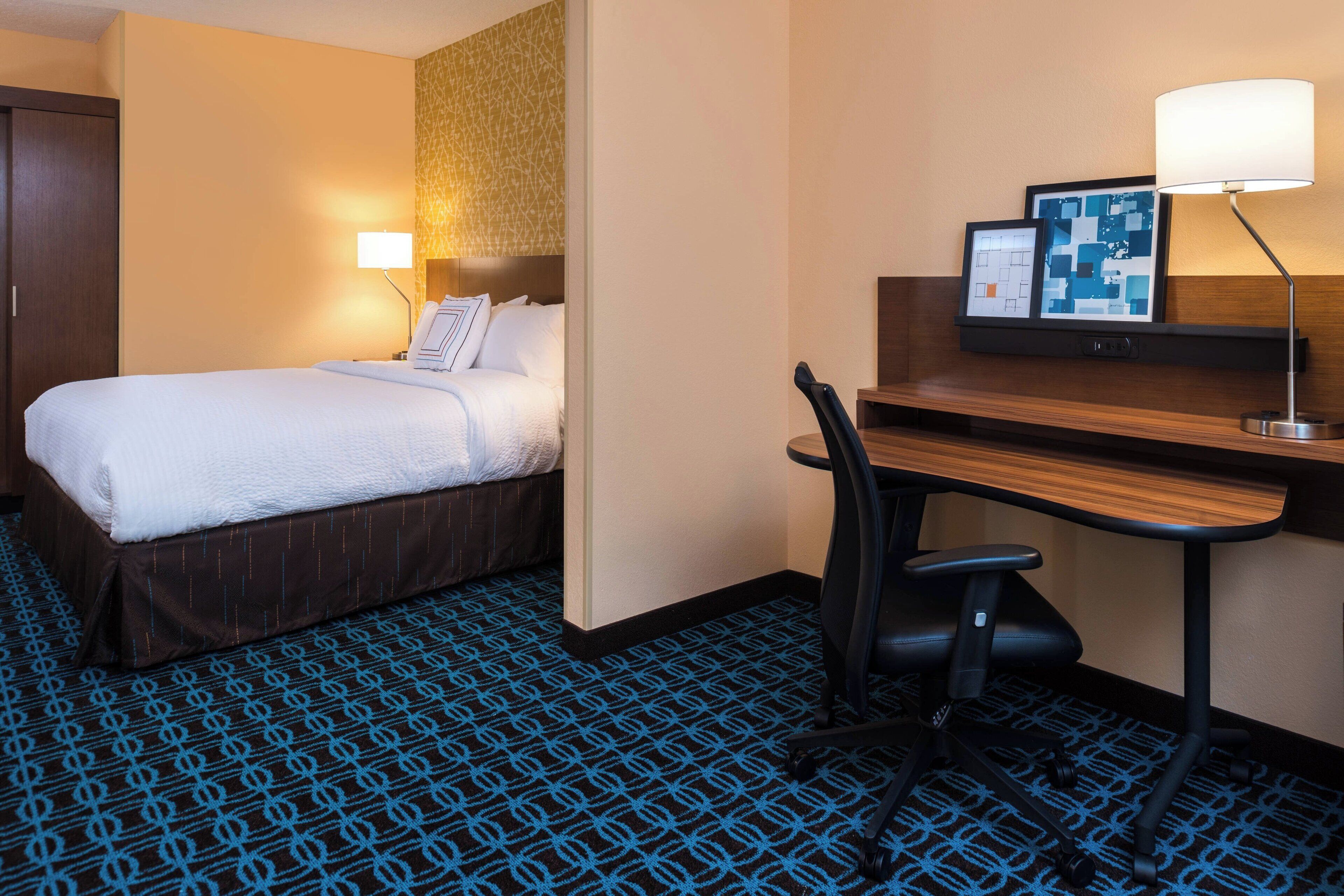 Ein Hotelzimmer mit Bett, Schreibtisch, Stuhl, Lampe und einer Karte an der Wand.