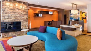 Un hall d’hôtel moderne avec un mur en pierre, un canapé bleu, une table ronde et un comptoir d’accueil.