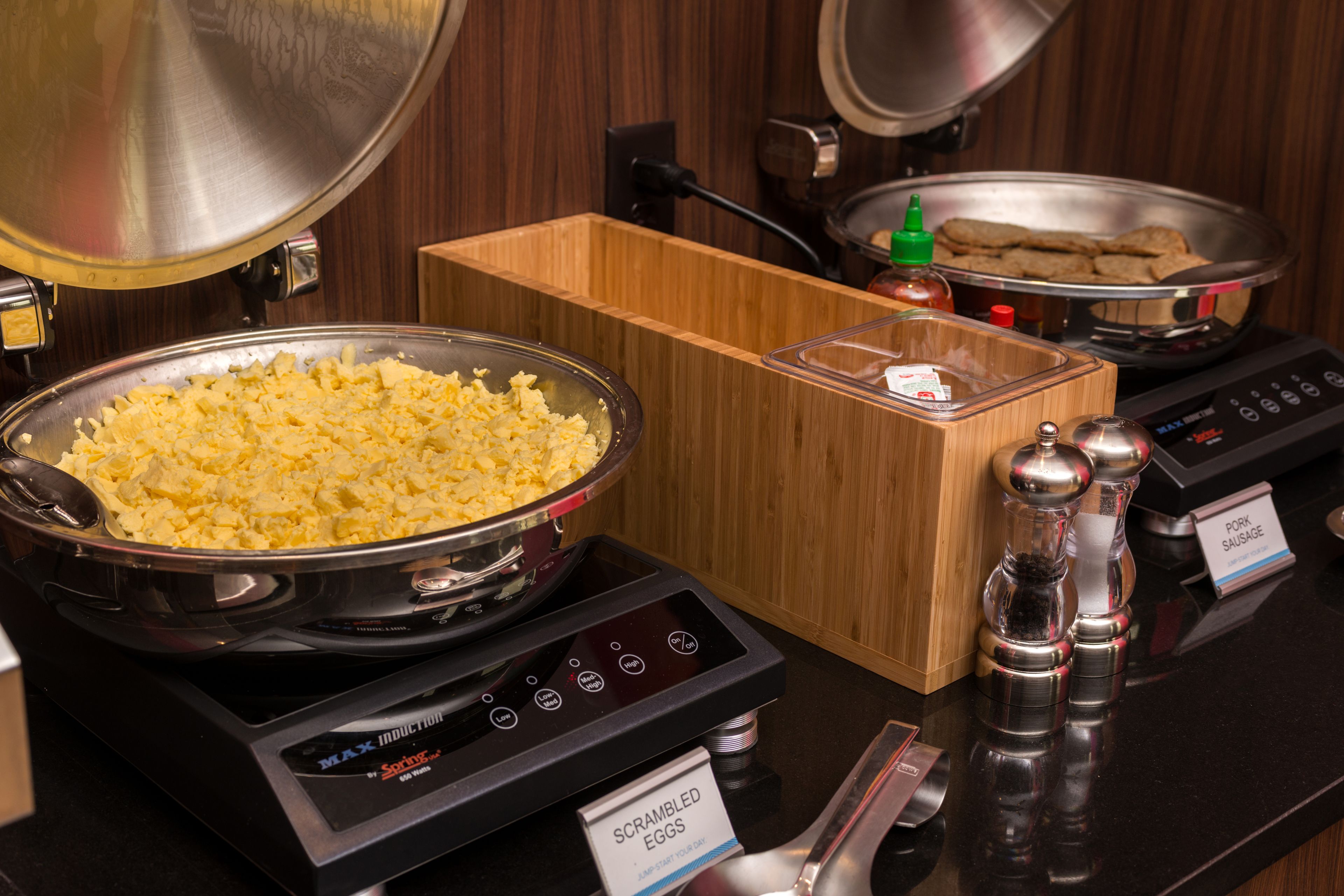 Scrambled eggs, sausages, and a grater on a buffet table.