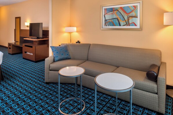 Une chambre d’hôtel avec un canapé, deux petites tables, un téléviseur, une lampe et un tapis à motifs.
