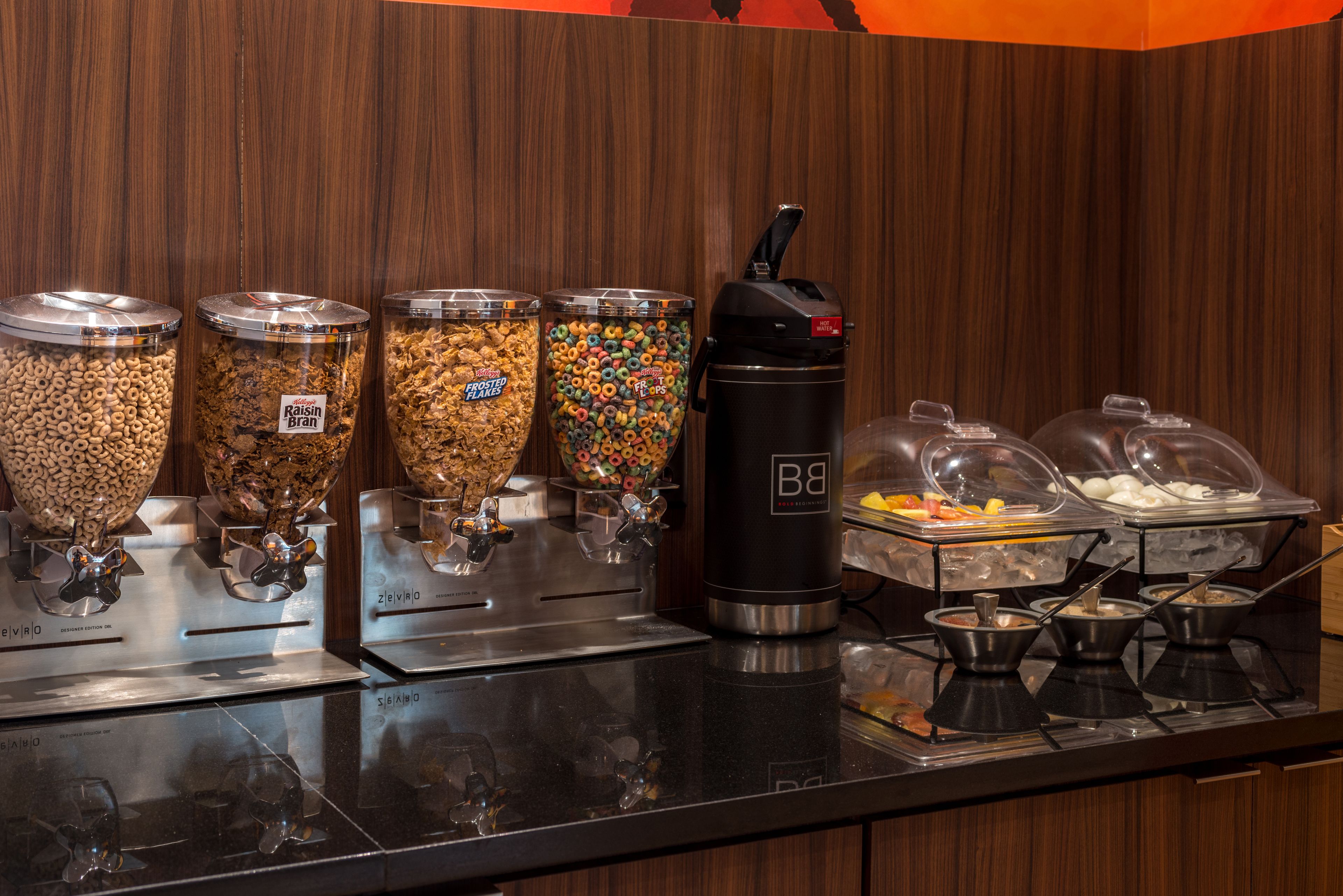 Zona de bufé con diferentes dispensadores de comida, incluyendo cereales, granola y yogur.