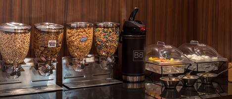 Zona de bufé con diferentes dispensadores de comida, incluyendo cereales, granola y yogur.