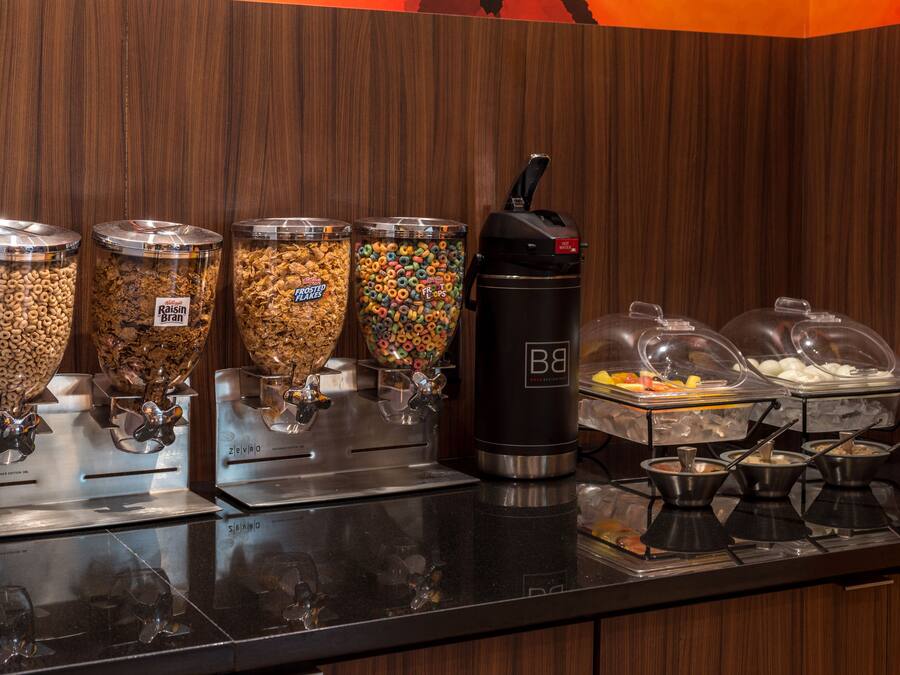 A buffet area with various food dispensers, including cereal, granola, and yogurt.