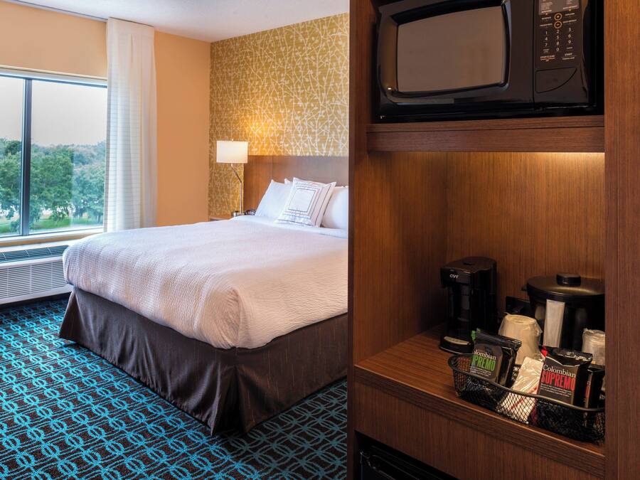 A hotel room with a large bed, a window with curtains, a wall-mounted microwave, and a coffee maker on the counter.