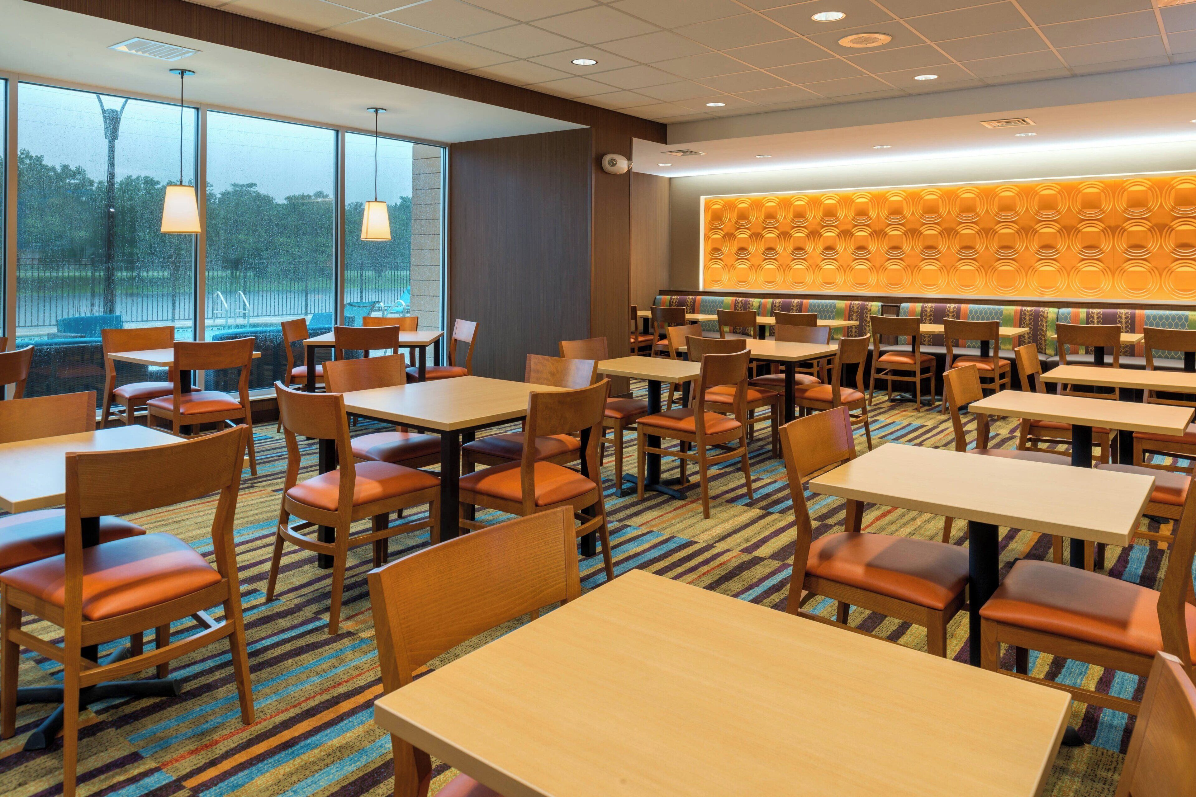 A restaurant with multiple tables and chairs, large windows, and a patterned wall.