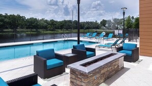 Un espace aménagé au bord de la piscine, avec des chaises longues, un foyer en pierre et une vue sur un lac.