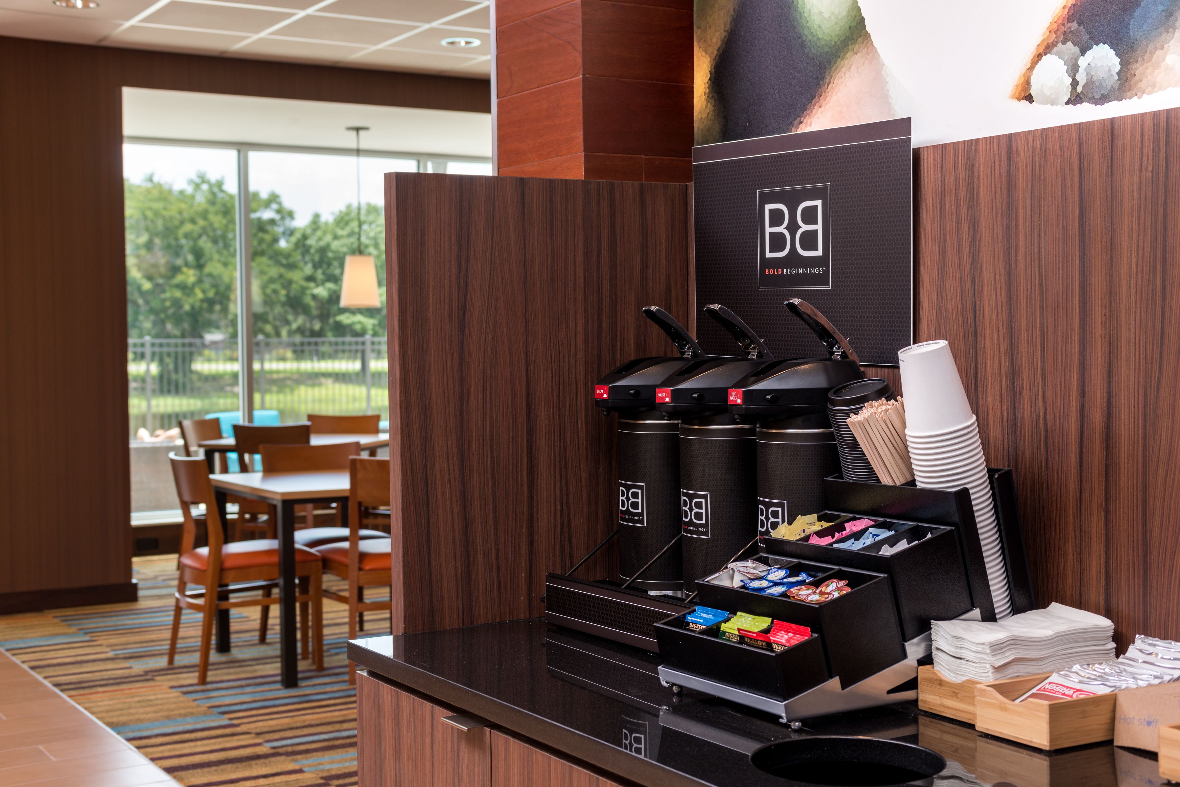 A coffee station with multiple dispensers, a menu board, and a seating area with tables and chairs.