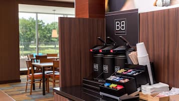 A coffee station with multiple dispensers, a menu board, and a seating area with tables and chairs.