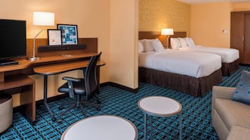 Quarto de hotel com uma escrivaninha, duas camas, uma TV e um pequeno espaço para sentar.