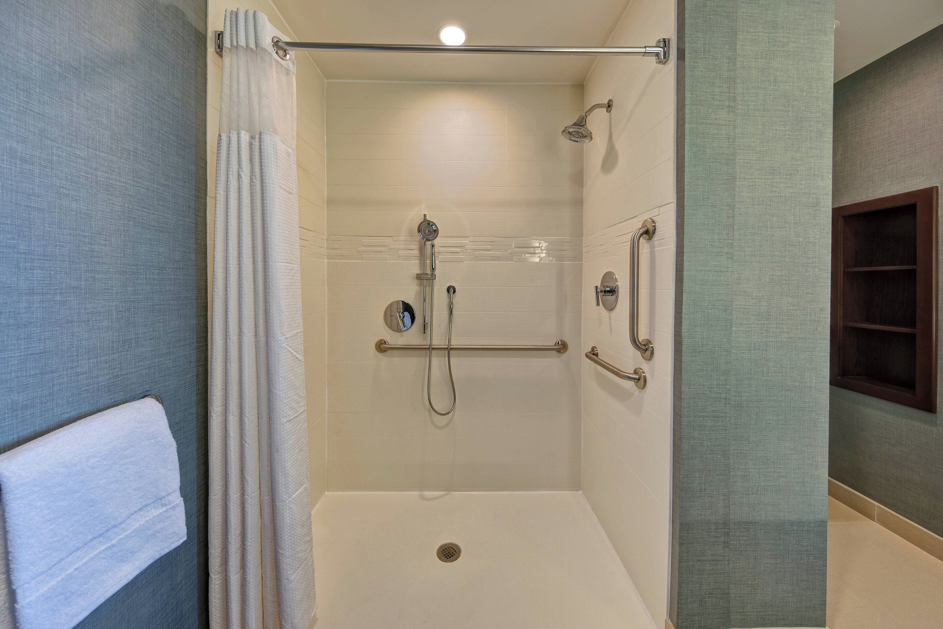 A walk-in shower with a grab bar, a handheld showerhead, and a floor drain.