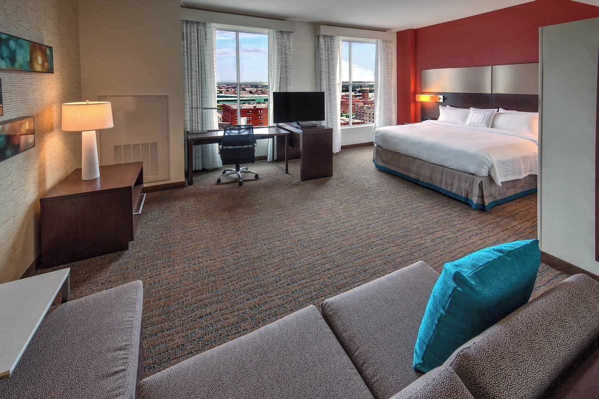 Habitación de hotel con cama, escritorio, computadora, televisor y vista de la ciudad.