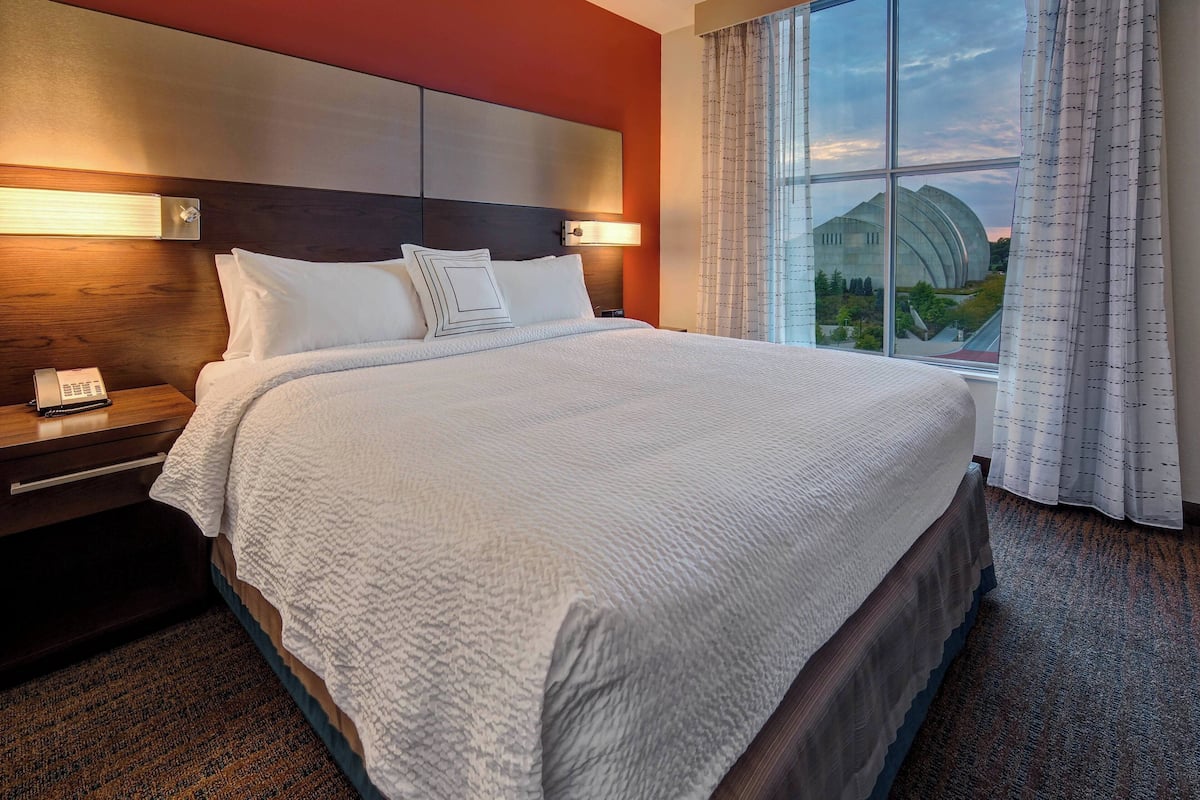 Habitación de hotel con una cama grande, un teléfono en la mesita de noche y vistas a un edificio a través de la ventana.