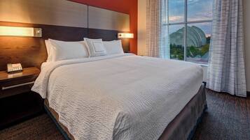 A hotel room with a large bed, a bedside telephone, and a view of a building through the window.