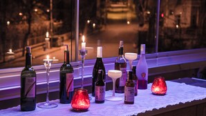 Una mesa con varias botellas y copas, velas y vista a una calle por la noche.