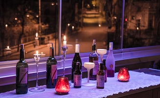 Una mesa con varias botellas y copas, velas y vista a una calle por la noche.