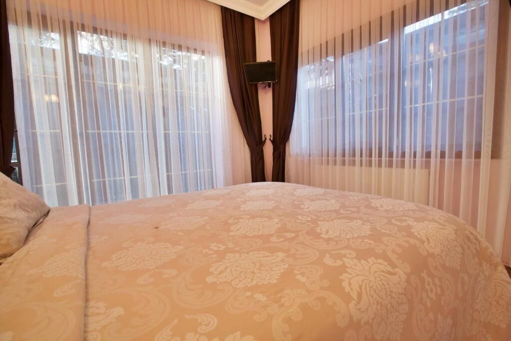 A bedroom with a large bed, sheer curtains, and a mounted TV.