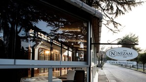 A cafe and restaurant with a glass facade, outdoor seating, and a sign indicating it is Nizam. - Nizam Butik Otel Buyukada (Adalar)