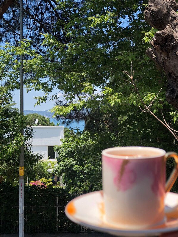 A cup of coffee on a saucer, with a view of a building and trees in the background.