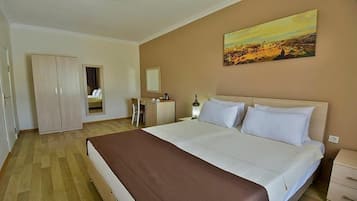 Una habitación de hotel con una cama grande, un armario, un escritorio, una silla, un espejo y un cuadro en la pared.