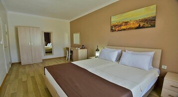 Una habitación de hotel con una cama grande, un armario, un escritorio, una silla, un espejo y un cuadro en la pared.