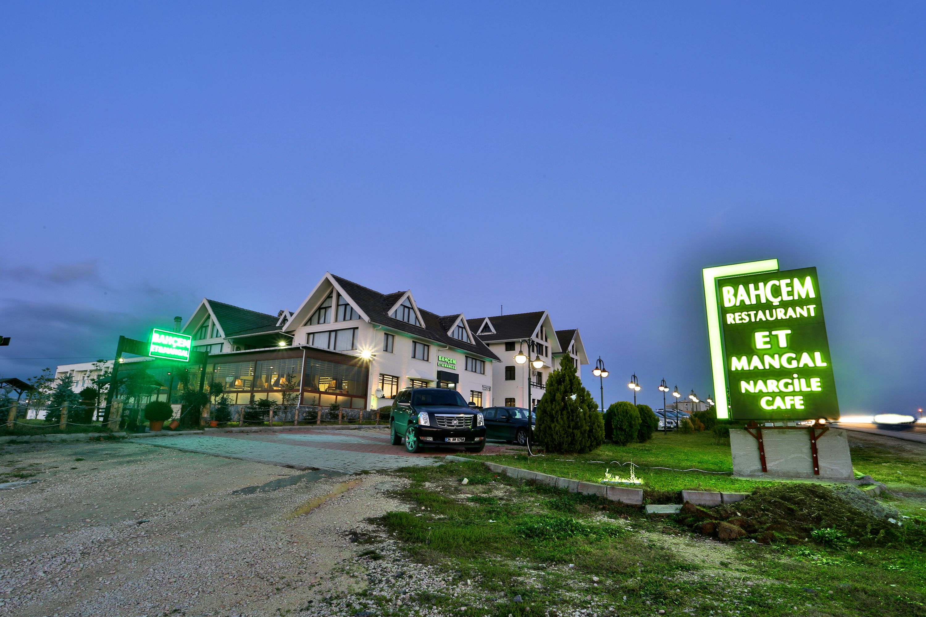 A restaurant with a sign reading "BAHÇEM RESTAURANT ET MANGAL NARCILE CAFE" in front of a building with a green-lit sign.