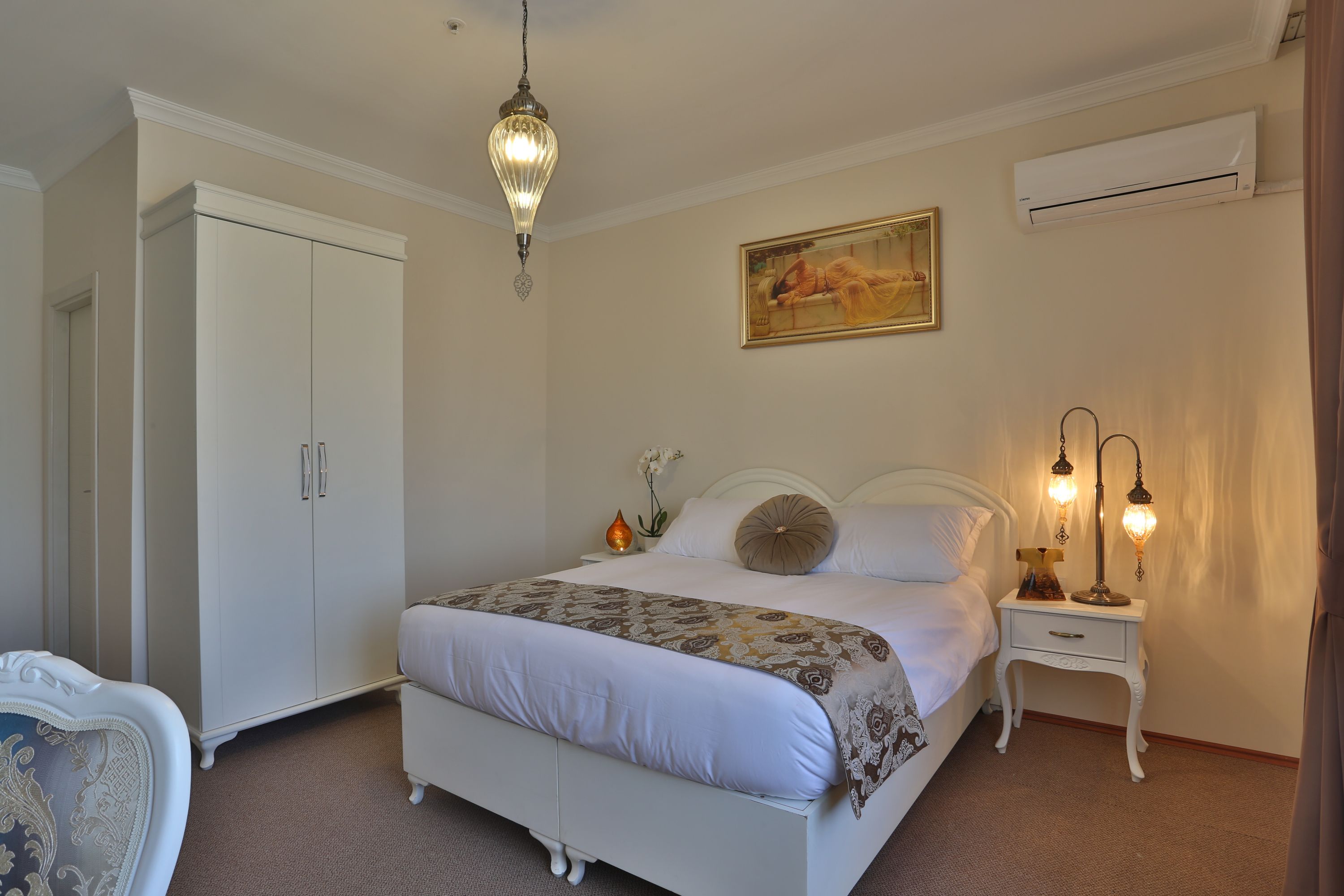 A bedroom with a bed, bedside table, lamp, air conditioning unit, and a wardrobe.