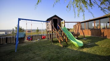 Children can play on the slide and swing set in this playground area surrounded by a grassy lawn and a wooden fence.